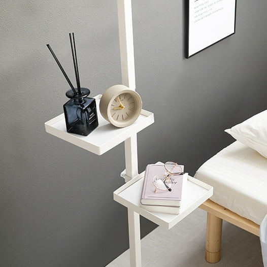 四角いトレイの突っ張りポールラックがベッド横に設置されていて本や時計が置かれている