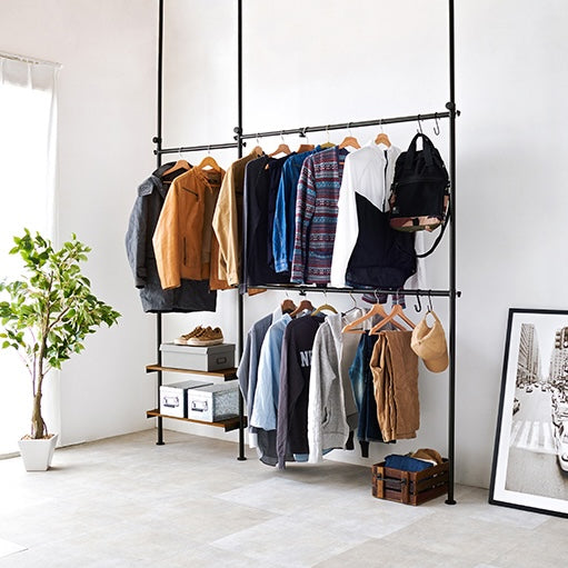 ブラウンの突っ張り伸縮ハンガーラックに沢山の洋服をかけている様子