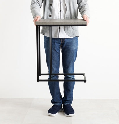 コンクリ風デザインのサイドテーブルを男性が持ち上げている様子