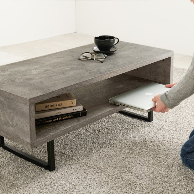コンクリート風のスタイリッシュなローテーブルの収納部分に本やパソコンをしまっている様子