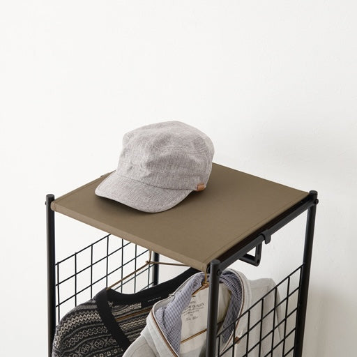 ブラウンのスリムなハンガーラックの上部に帽子を置いている様子