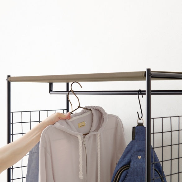 ブラウンのファブリック収納付きハンガーラックに洋服をかけようとしている様子