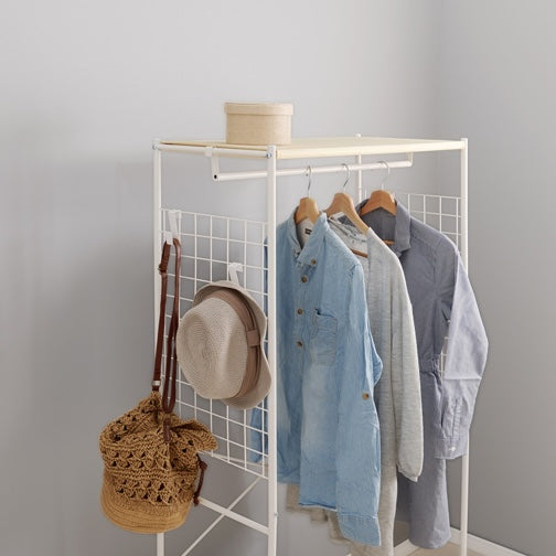 ホワイトのファブリック収納付きハンガーラックに洋服や帽子、バッグをかけている様子
