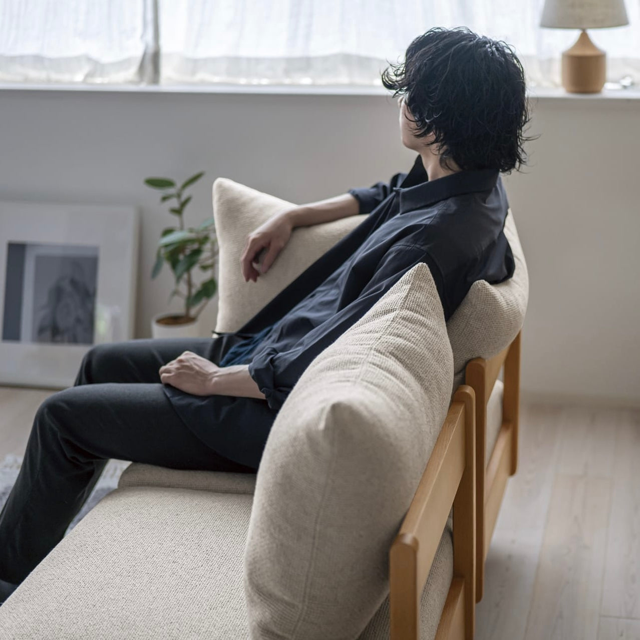 木製フレームのベージュのソファに人が座っている様子