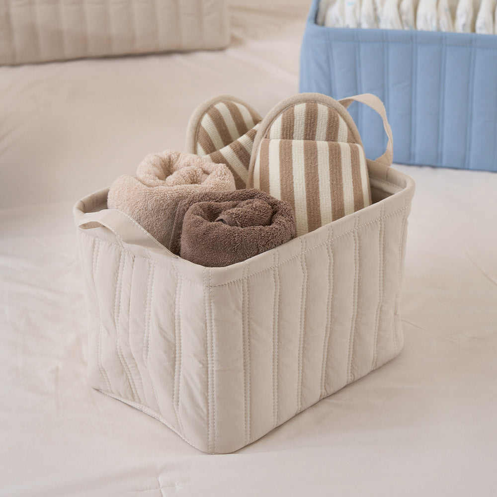キルティング素材のベージュのバスケットにタオルやスリッパが収納されている様子