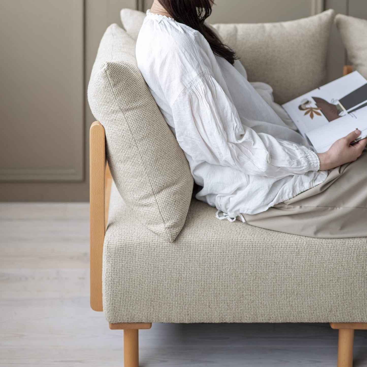 木製フレームのベージュのソファに人が座っている様子