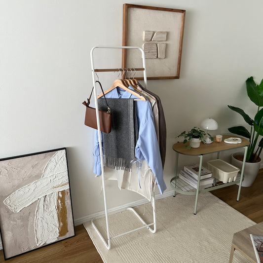 スチールと木製バーのハンガーラックに茶色のバッグと洋服がかかっている様子