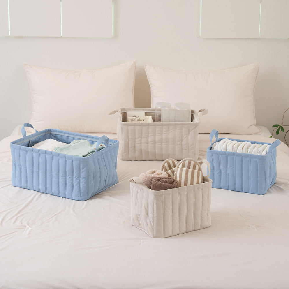 ブルーとベージュのキルティング素材の2サイズのバスケットがベッドに置かれている様子