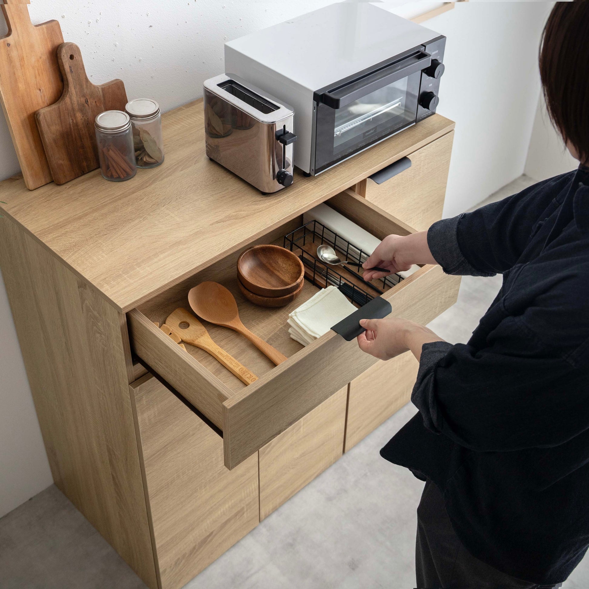 幅90cmのライトウッドキッチンシェルフで開いた引き出しに木製調理器具とワイヤーバスケット収納付き