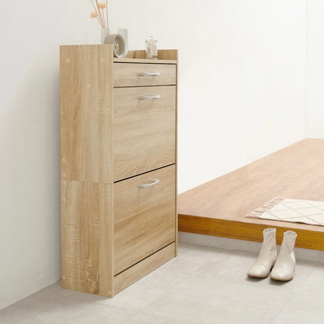 ナチュラルのフラップ扉式のシューズケースを玄関に置いている様子