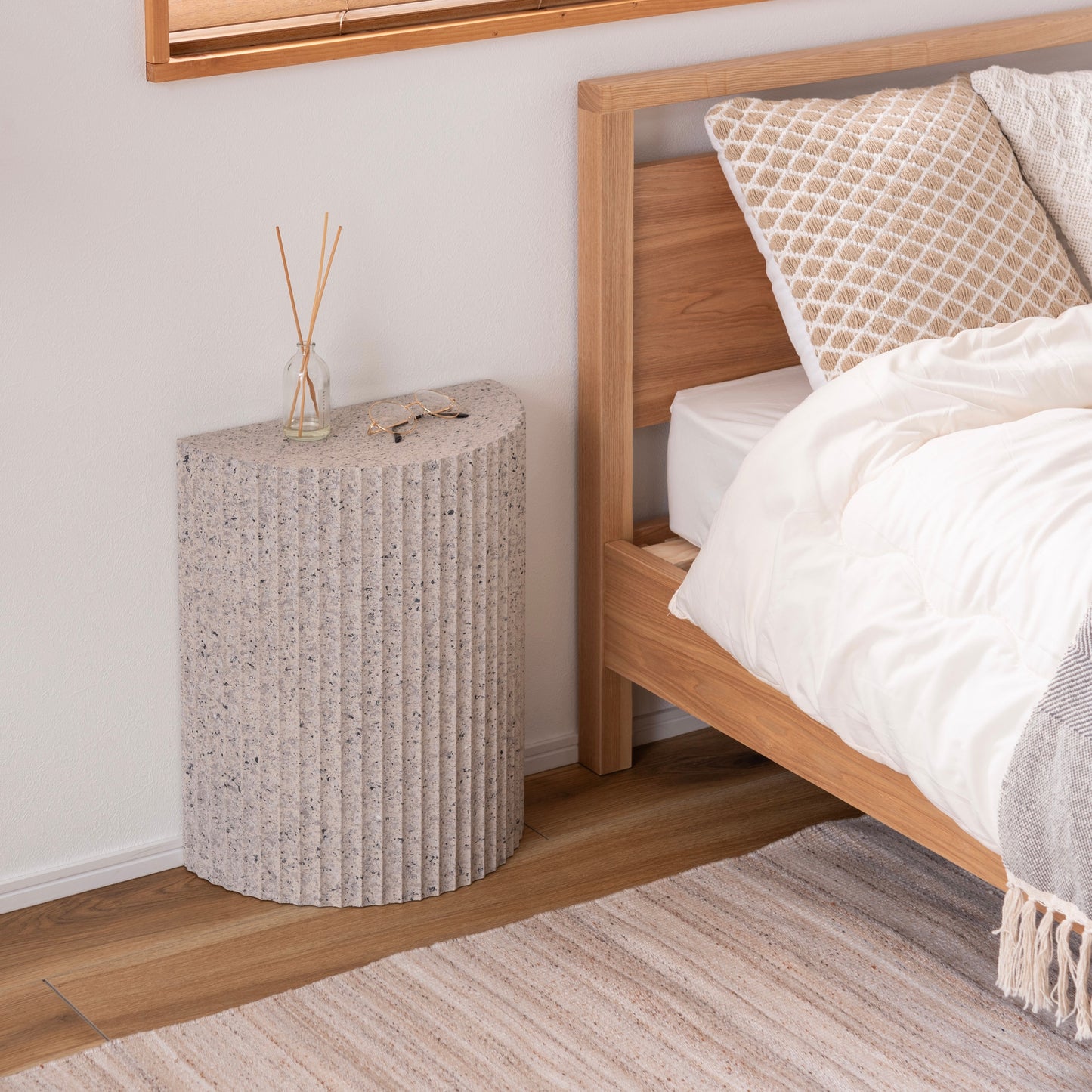 テラゾー柄の半円のスツールがベッドサイドに置かれている様子