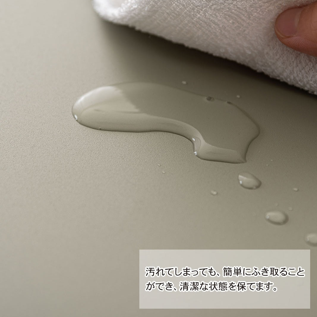 スチール製のペールグリーンのサイドテーブルにこぼれた水滴を布で拭き取っているところ