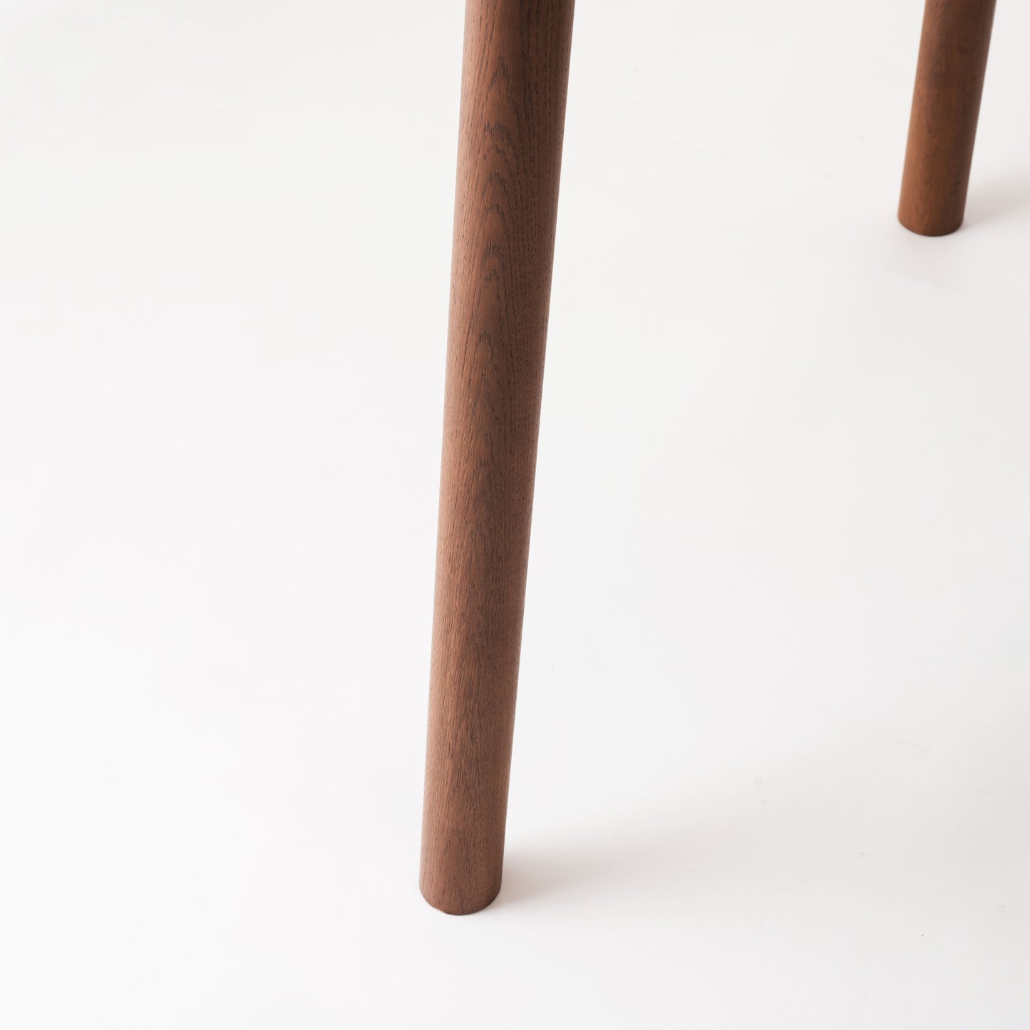 天然木オーク材を天板と脚部に使用しウレタン塗装で濃いブラウンに塗られたワントーンデザインのダイニングテーブルの脚の写真