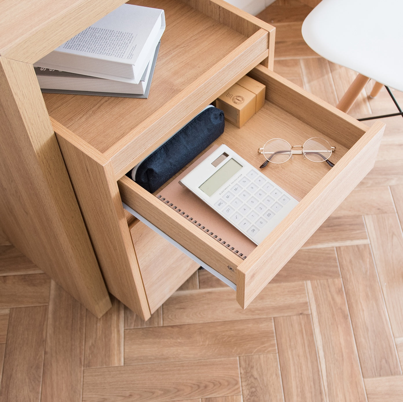 デスク下に置かれた木目調のサイドチェストに文具やメガネが収納されている様子