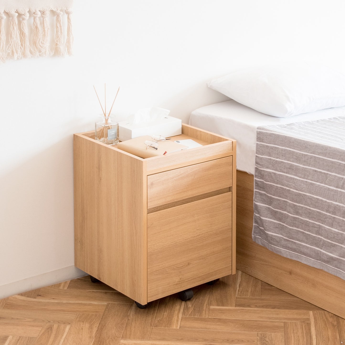 ベッドサイドに置かれた木目調のサイドチェストにティッシュケースやフレグランスが置かれている様子