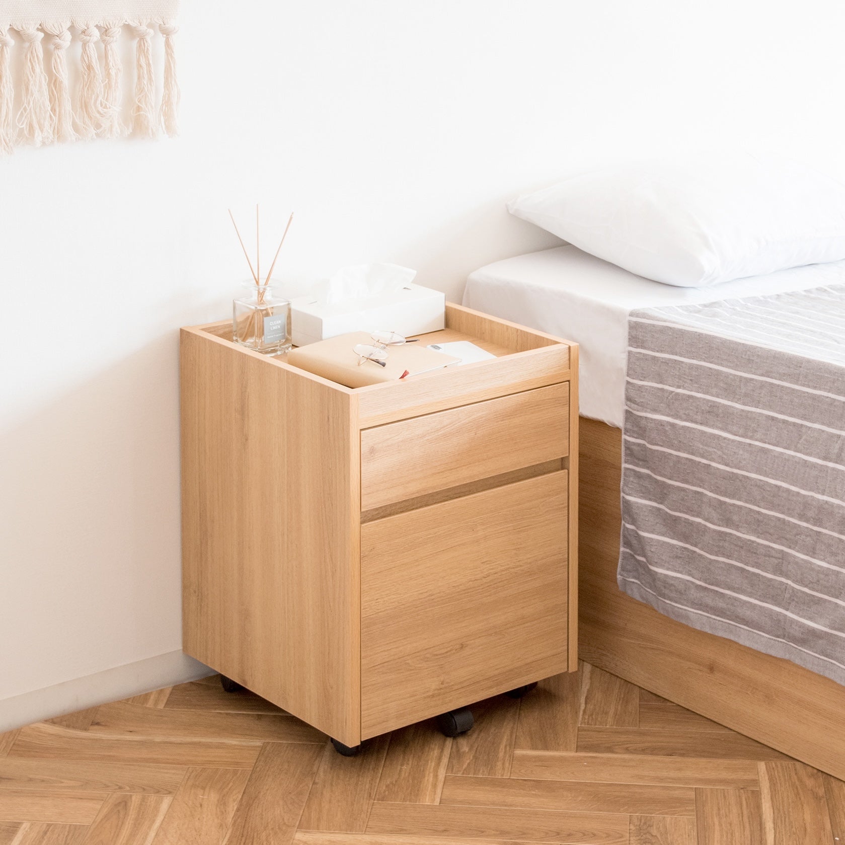 ベッドサイドに置かれた木目調のサイドチェストにティッシュケースやフレグランスが置かれている様子