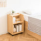 ベッドサイドに置かれたキャスター付きの木目調の2段のラックに本やティッシュケースなどが収納されている様子