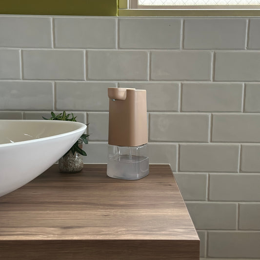 ベージュとクリアのシンプル泡ソープディスペンサーを洗面台に置いている様子