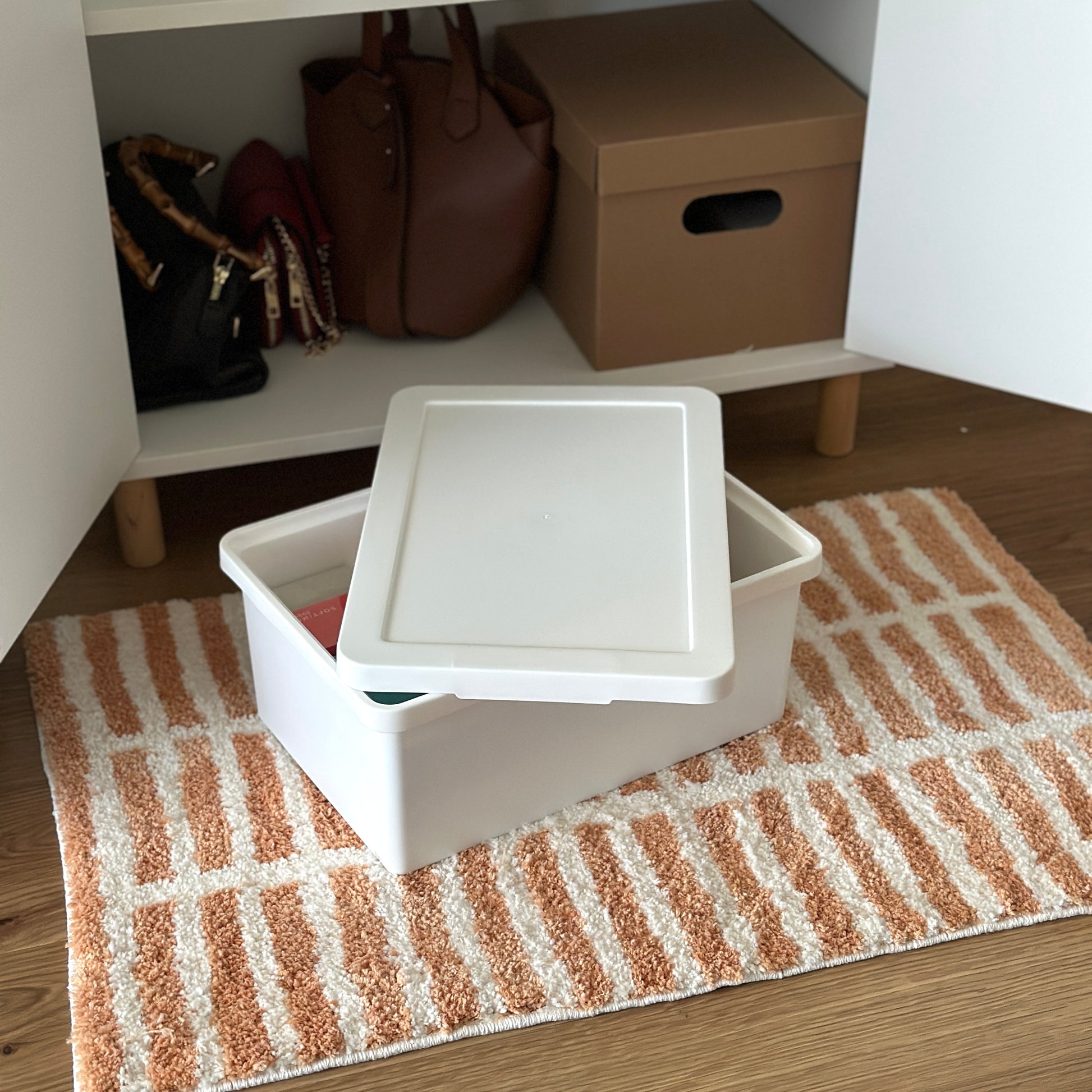 蓋付きのシンプルなプラスチックの収納ボックスが棚の前に置かれている様子