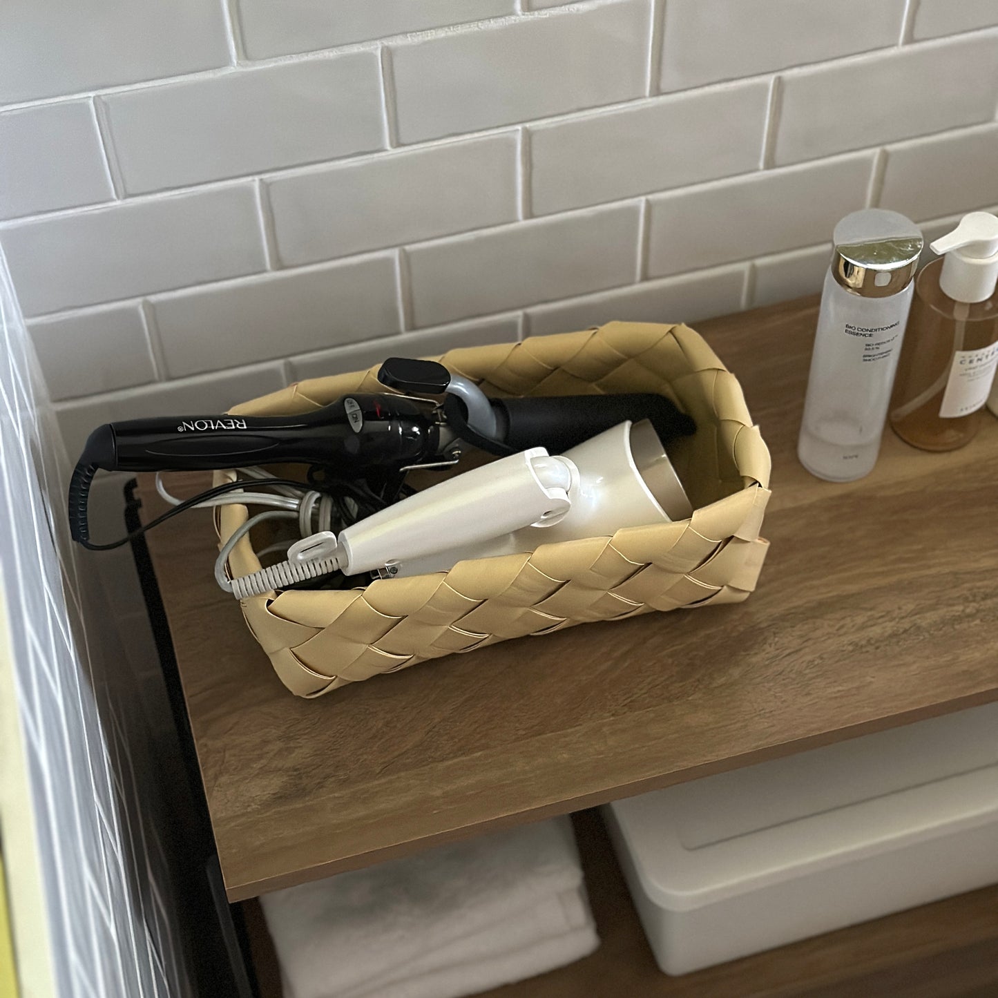 洗面所で手編みのバスケットにドライヤーとコテを収納している様子