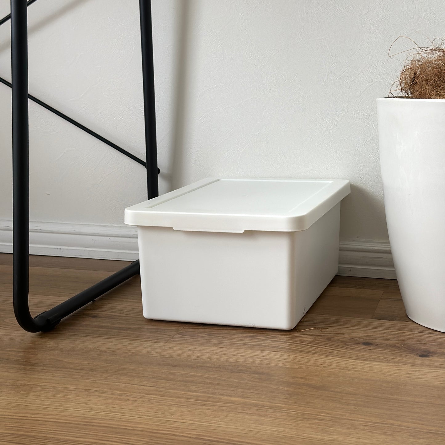 蓋付きのシンプルなプラスチックの収納ボックスがデスクの下に置かれている様子