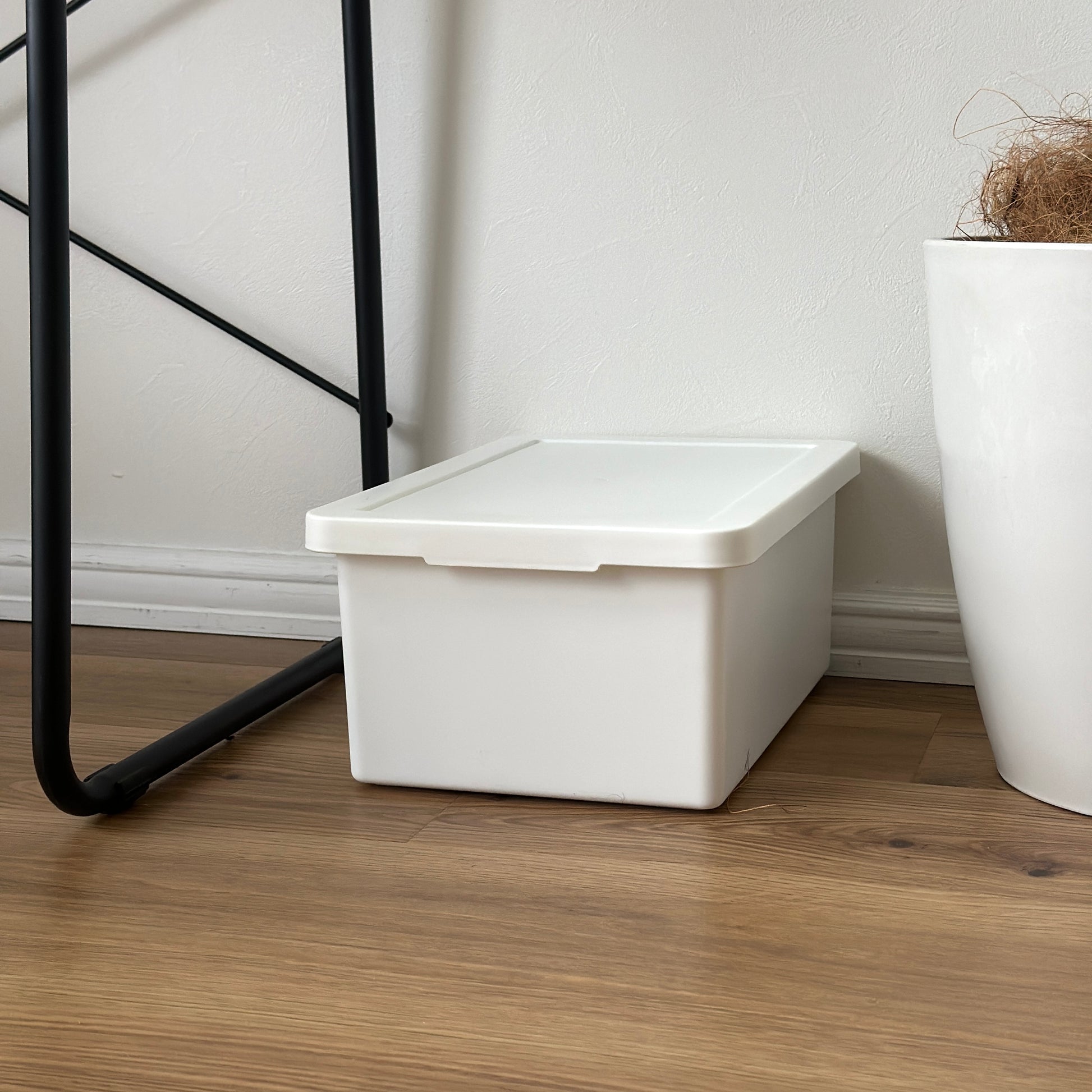 蓋付きのシンプルなプラスチックの収納ボックスがデスクの下に置かれている様子