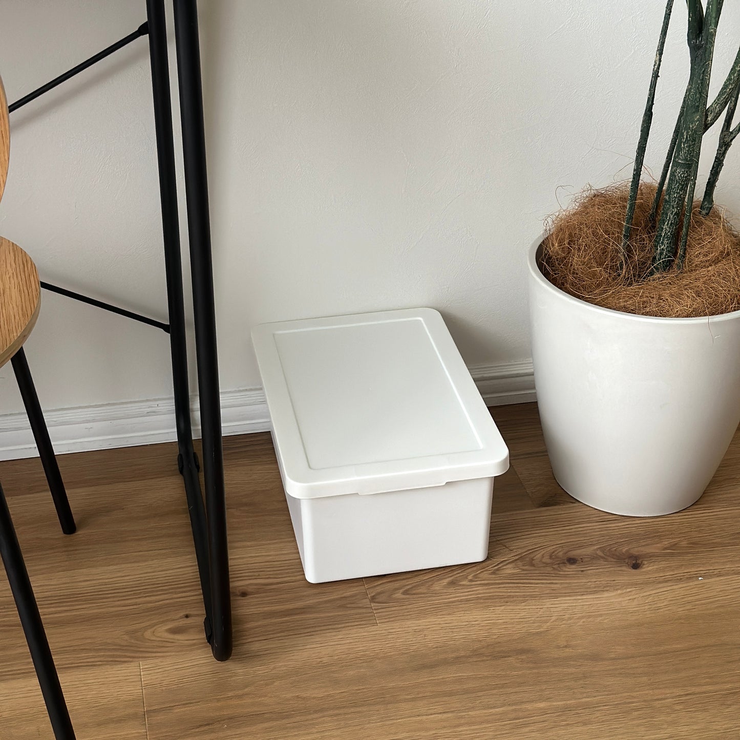 蓋付きのシンプルなプラスチックの収納ボックスがデスクの下に置かれている様子