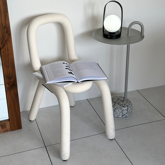 針金を曲げたようなユニークなデザインの白い椅子の上に本が2冊置かれていて、横のテーブルにはライトが置かれている