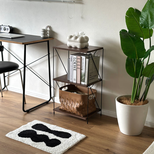 木目のウッドと細いブラックフレームの２段のオープンシェルフに雑誌やティッシュケース、茶色の収納ボックスが置かれている様子