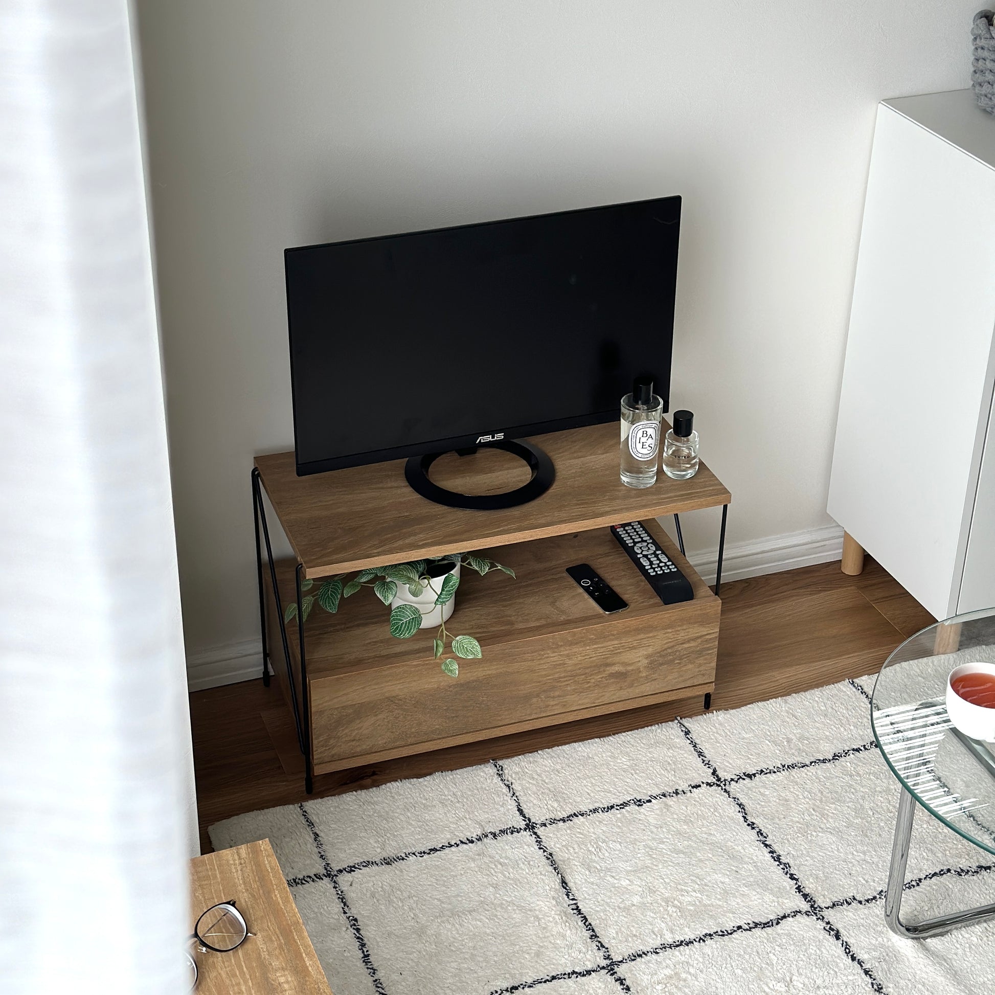 木目のウッドと細いブラックフレームのテレビボードを部屋の隅に置いている様子