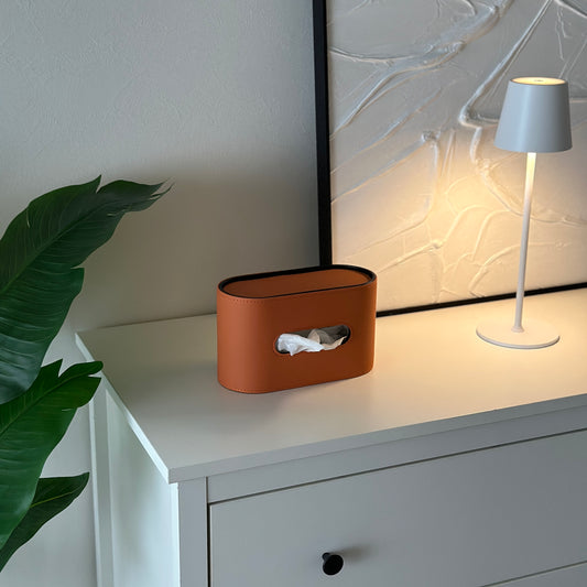 棚の上に置いてあるオレンジのレザー調デザインの楕円型ティッシュケース