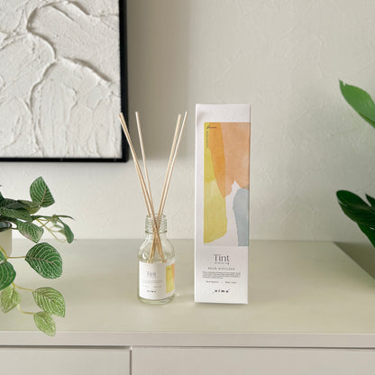 部屋の中の白い棚の上にリードディフューザーのとそのパッケージ箱が並んで飾られている様子