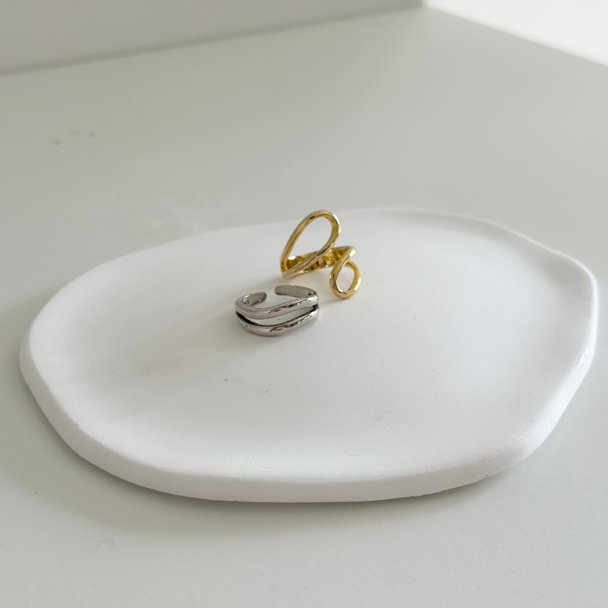 石膏でできたプレートの上に置かれたゴールドのリングと2周のデザインになっているシルバーリング