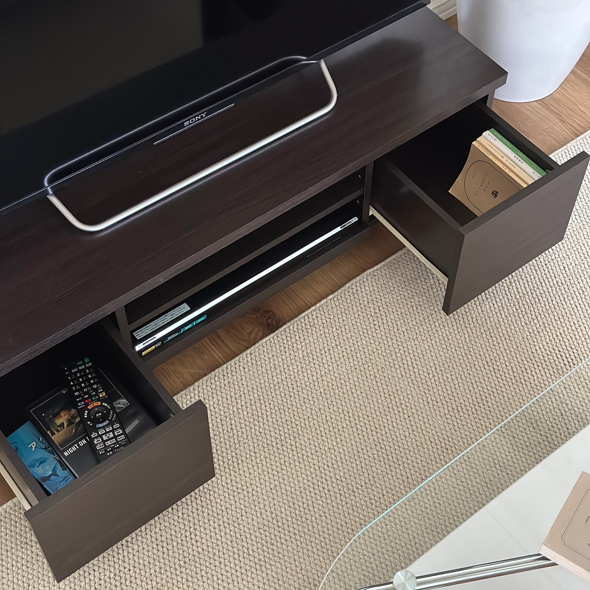 ダークブラウンのテレビボードの引き出し収納に文庫本やテレビのリモコン、DVDが入れられている