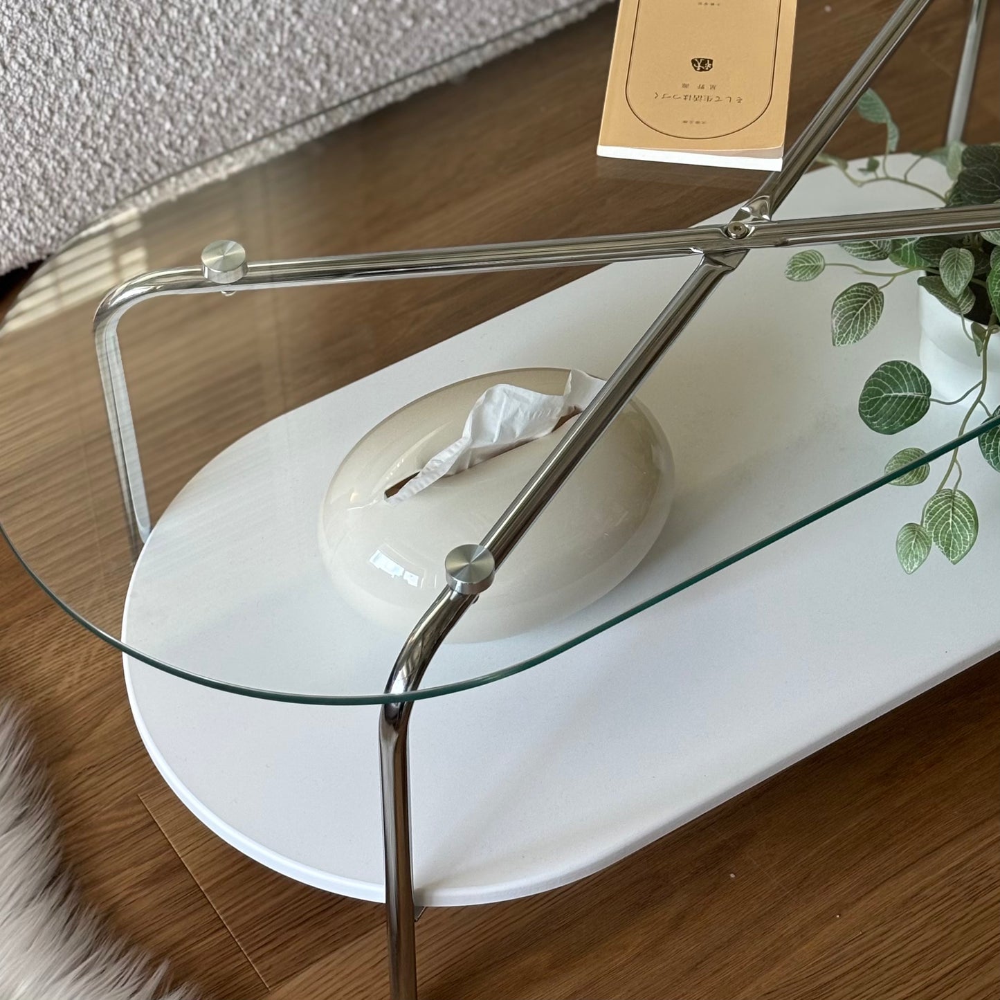 光沢のある丸みを帯びたベージュのティッシュケースを透明のテーブルに置いている様子