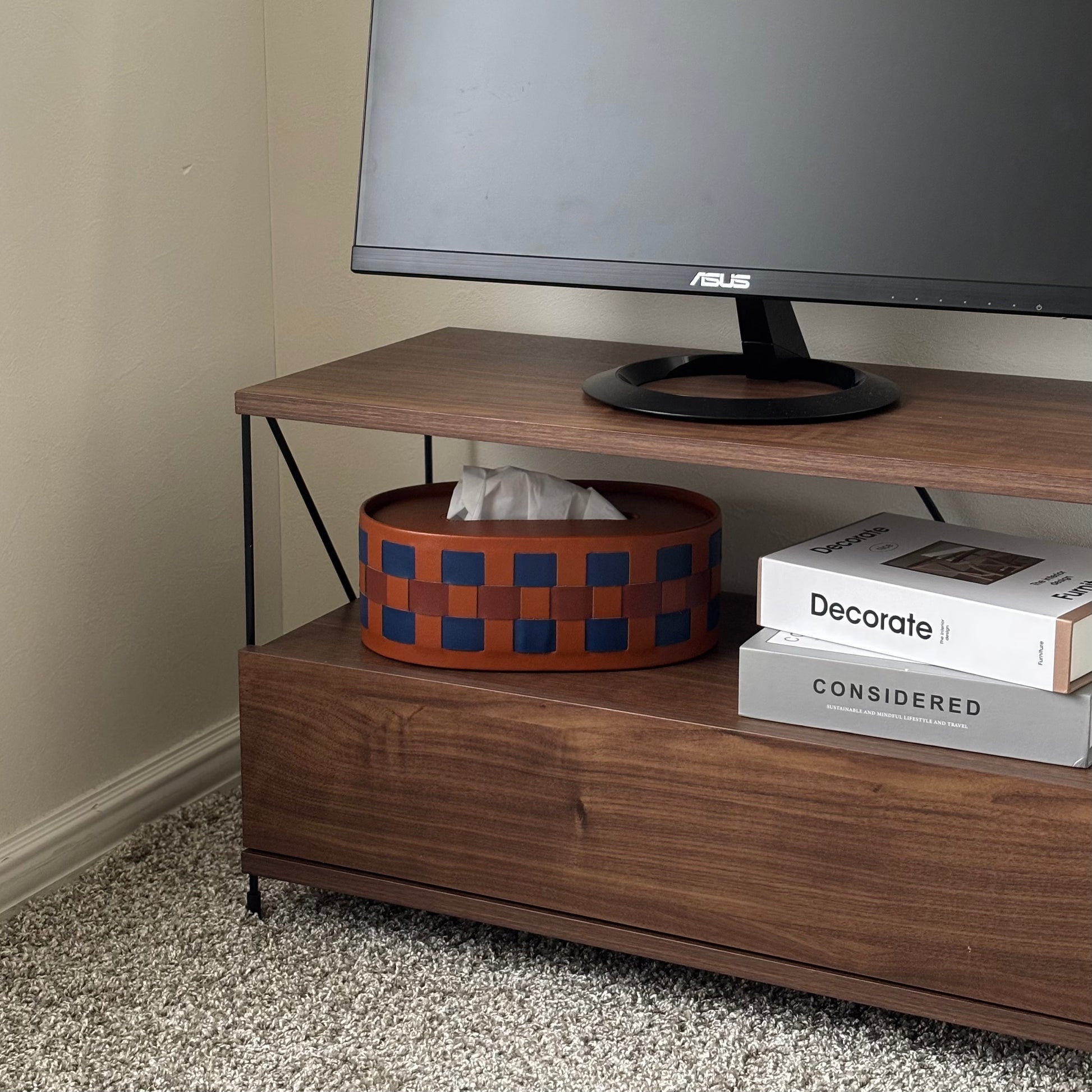 ブルーとブラウンの編み込みデザインのオーバル型のティッシュケースがテレビ台の収納部分に置かれている様子