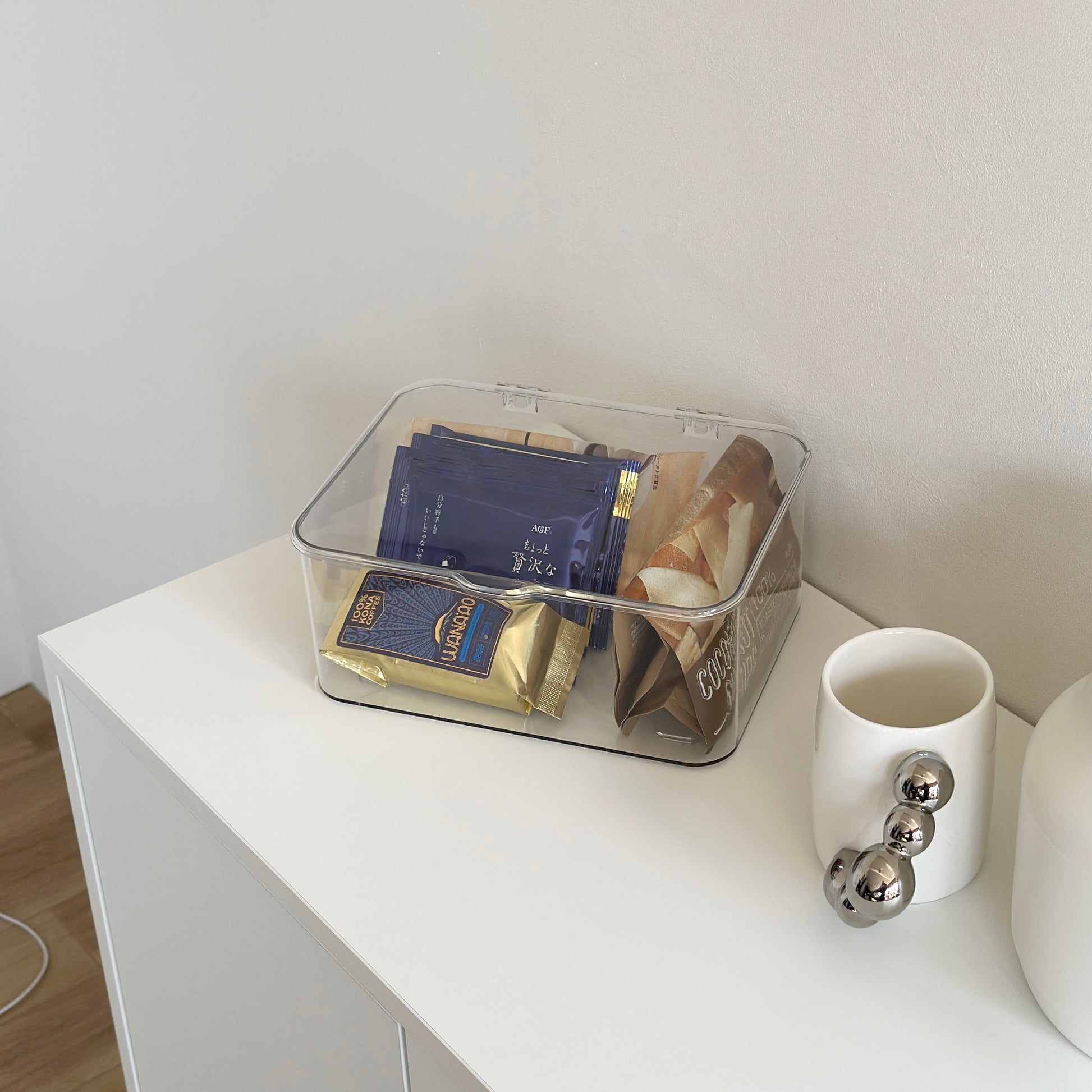 マグカップとケトルと透明のボックスの中にコーヒーバッグが白い棚の上にあるインテリア