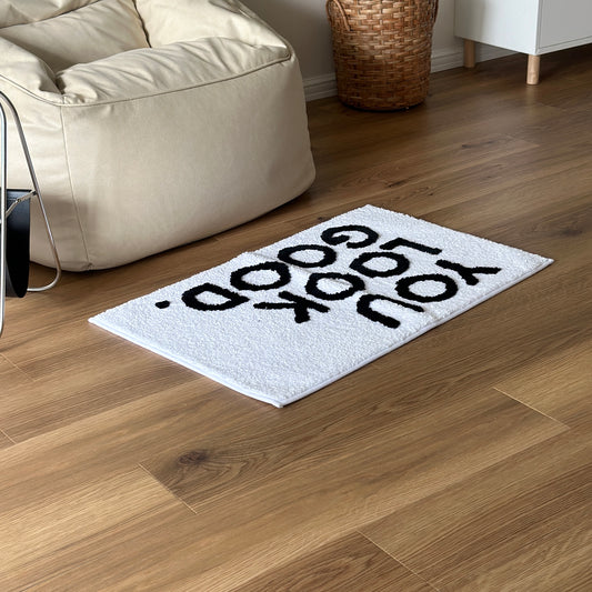 黒の文字が入った白いラグがソファの前に敷かれている様子