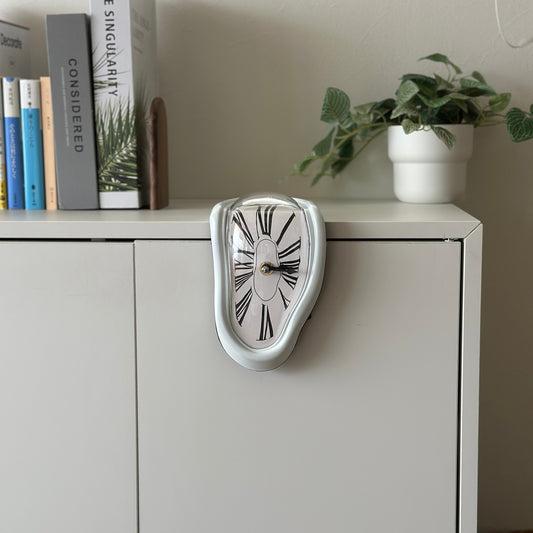 溶けたようなデザインが特徴のホワイトの置き時計を白い棚に置いている様子