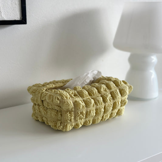 ポコポコしたキルティング素材のイエローのティッシュケースが白い棚の上に置かれている様子