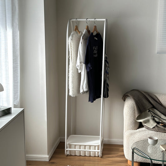 ホワイトのアーチ型のスタンドハンガーラックを部屋の隅に置いている様子