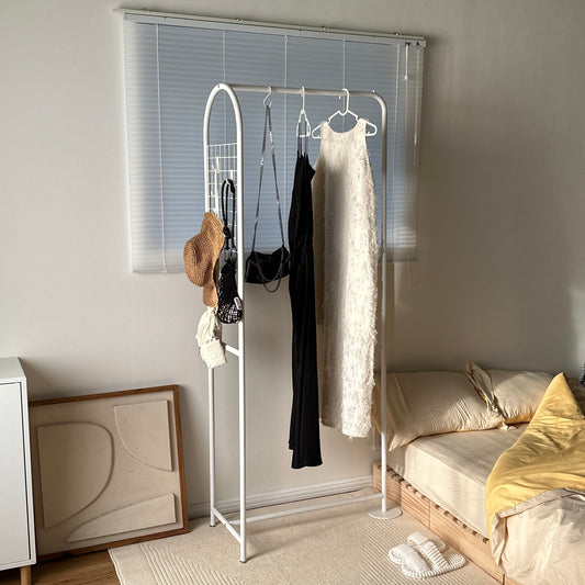 ホワイトのアーチ型のスチールハンガーラックにワンピースやバッグ、帽子がかかっている様子