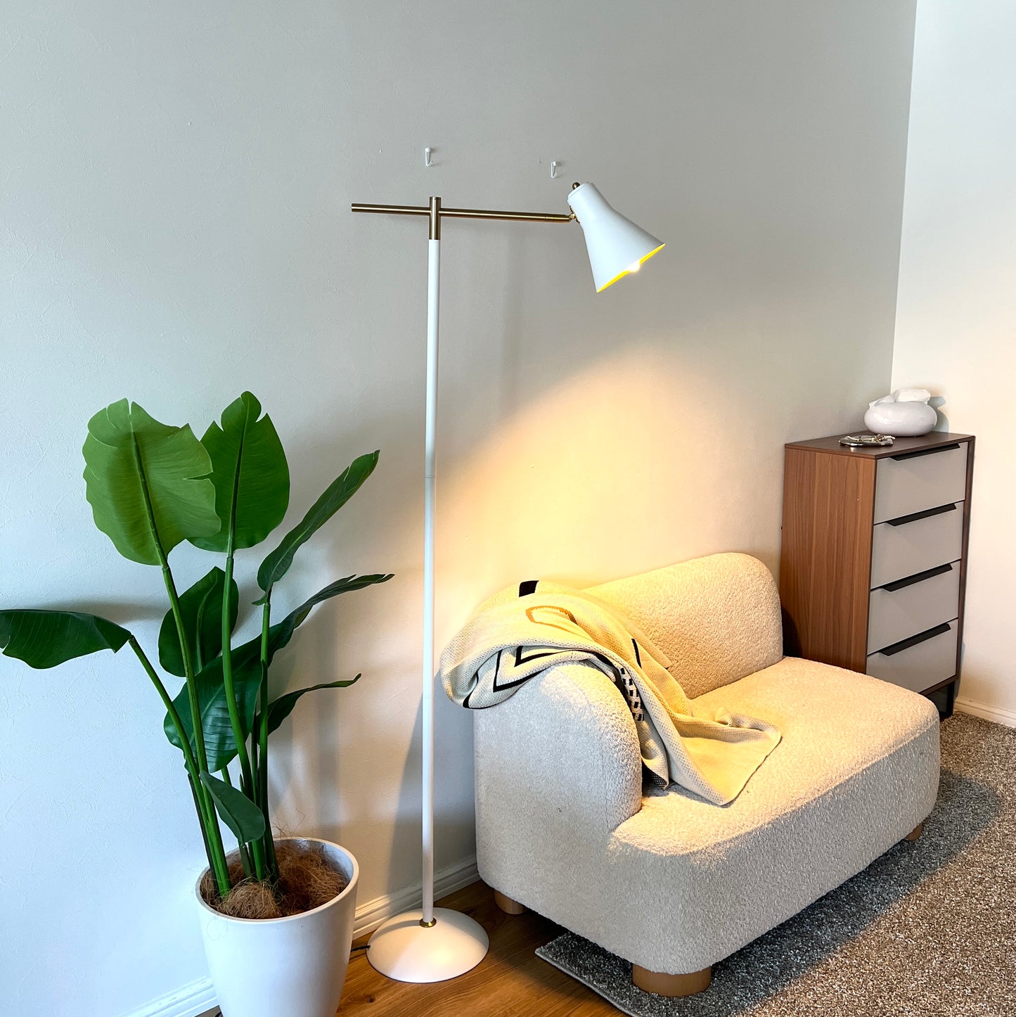 ホワイトのスチール製のフロアライトの電気をつけてソファ横に置いている様子