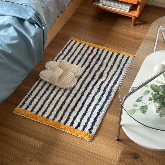 ブルーのボーダーとイエローの縁取りのミニラグをベッド横に敷いている様子