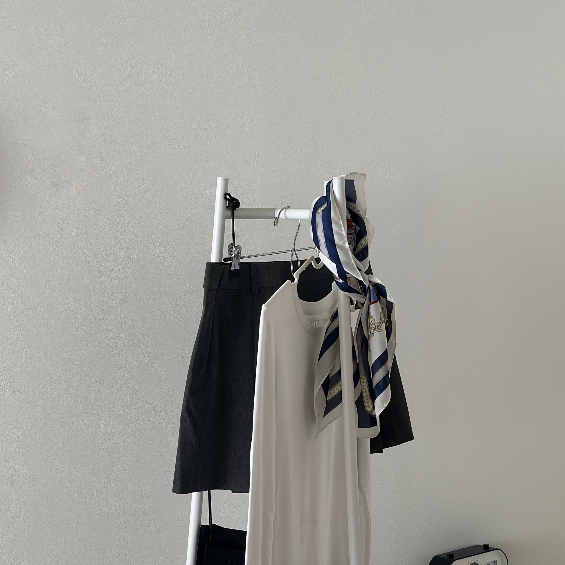 部屋の中で白いコンパクトでスタイリッシュなハンガーラックに洋服がかかっている様子