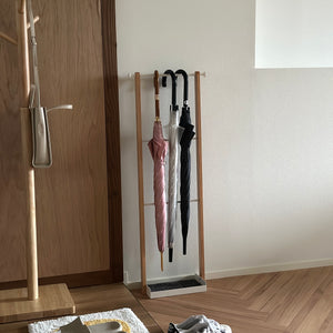 部屋の中に天然木とホワイトスチールの3段のアンブレララックが置かれており、ピンクの傘とビニール傘、黒の傘がかけられている。