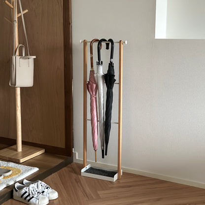 部屋の中に天然木とホワイトスチールの3段のアンブレララックが置かれており、ピンクの傘とビニール傘、黒の傘がかけられている。