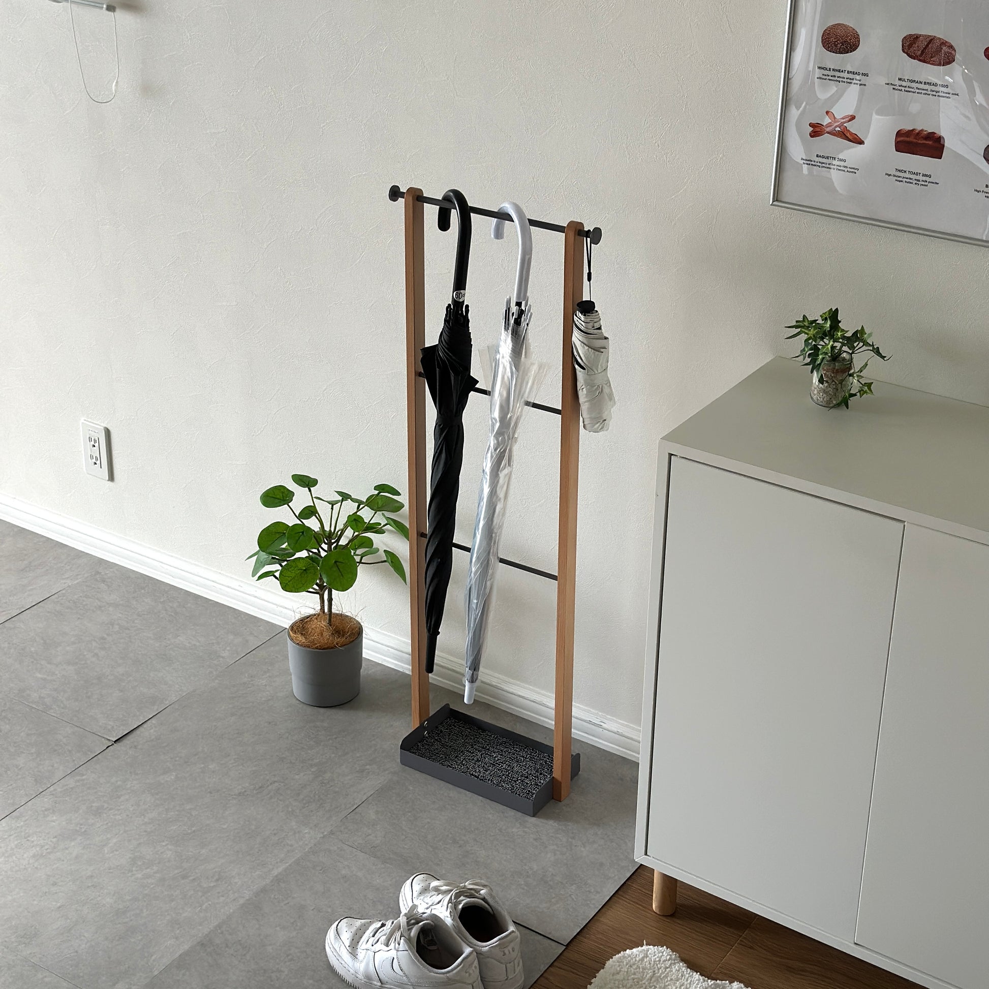 天然木とグレースチールの3段の傘立てに、ビニール傘と黒の傘がかけられている。