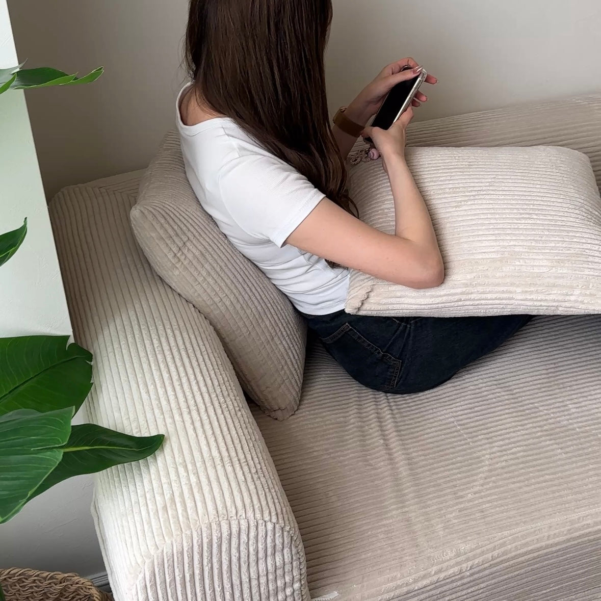 だらりんソファのベージュのコーデュロイ素材で女性が白いTシャツとジーンズに座ってスマホを持つ様子