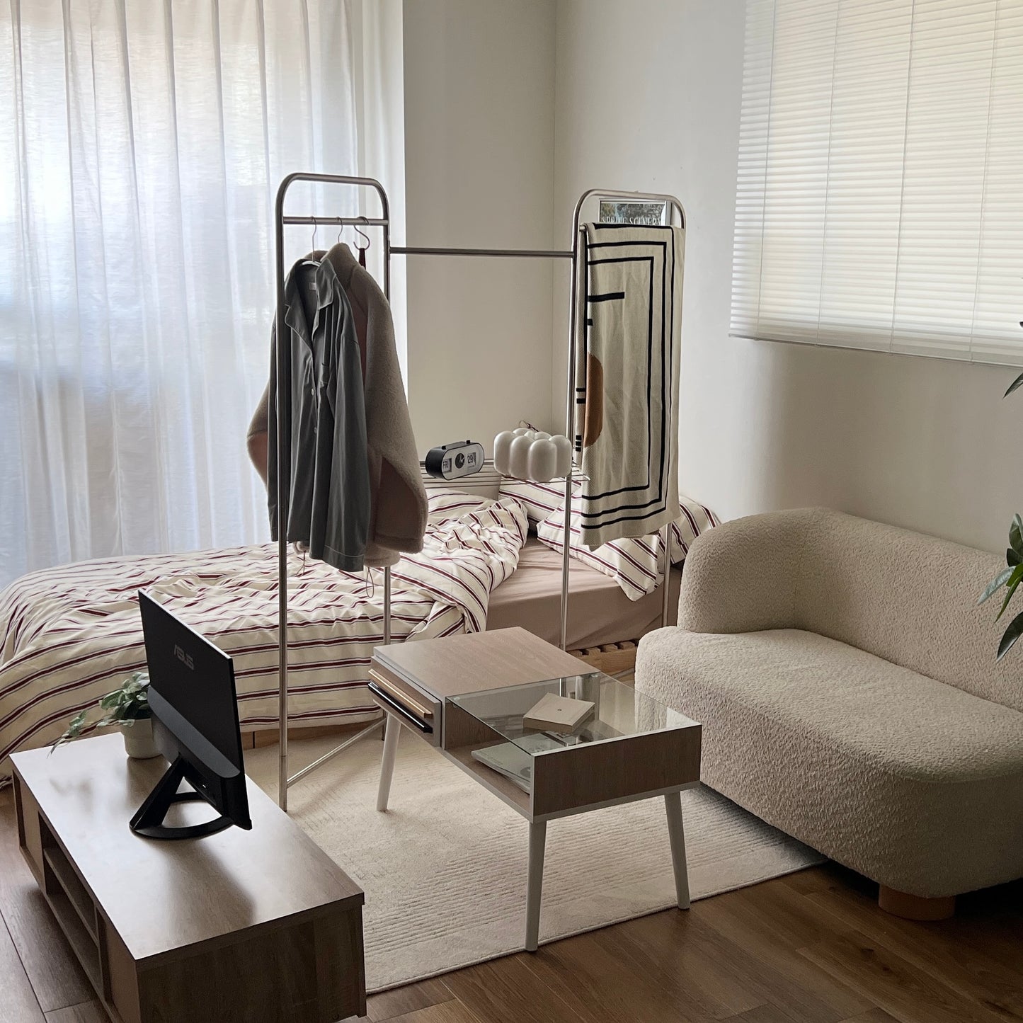 フォールディング式のパーテーションハンガーラックにブランケットをかけてベッドとリビングの間を間仕切りしている部屋